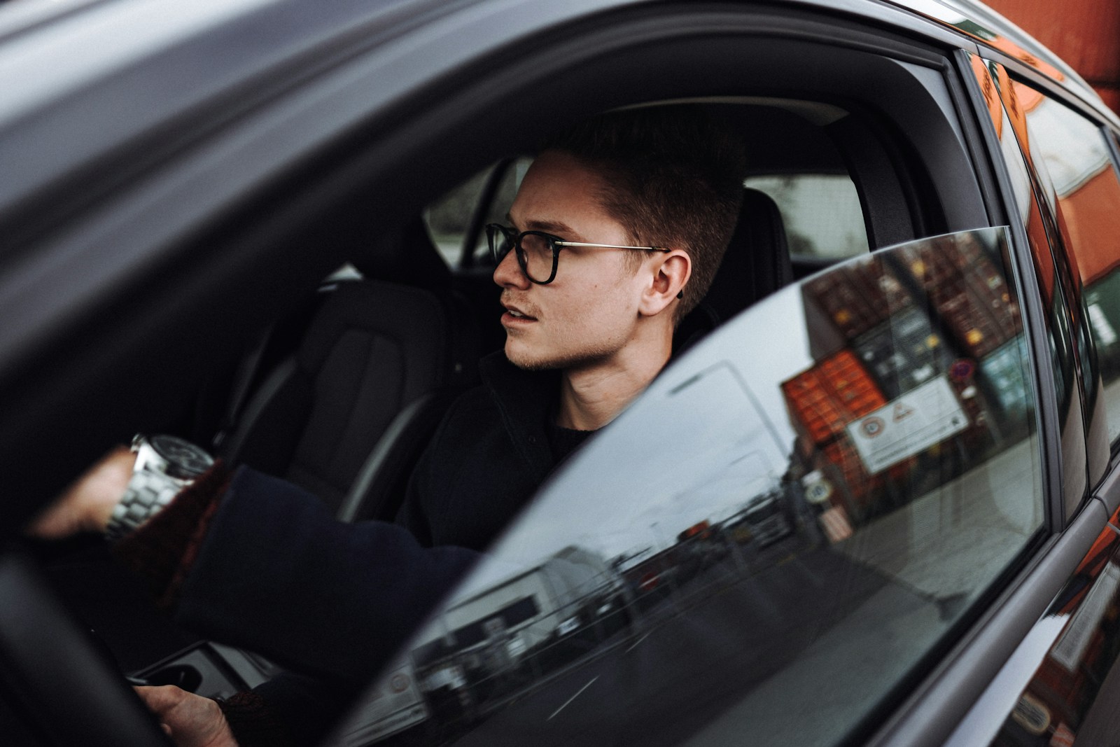 man in black jacket wearing eyeglasses sitting inside auto
